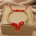 Elegant beaded bracelet with a red bow design and gold-tone beads on a red cord - Gold Bead Red Bow Bolo Bracelet (N-1111)