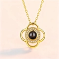 Golden flower projection necklace with dark gemstone and crystal halo on pink background - Gold Clover