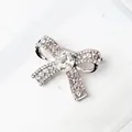 Silver bow brooch with sparkling white rhinestones on marble background for suit decoration - White