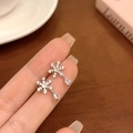 Boucles d'oreilles flocon d'argent avec goutte en zircone tenues dans un café cosy - Flocon de Neige Argenté avec Zirconia en Forme de Larme
