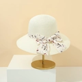 Dettaglio di un cappello di paglia crema a tesa larga con fiocco a fiori - crema