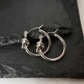Polierte silberne Knoten-Creolen aus 316L-Edelstahl auf einer schwarzen Steinfläche - Silber