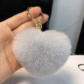 Close-up of fluffy grey rabbit fur heart keychain with a gold clasp held in hand - Light Gray