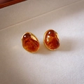 Close-up of amber resin earrings with irregular gold frames on a beige fabric background - Irregular Oval (Gold Plated)