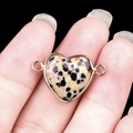 Dalmatian Jasper heart connector with gold trim held by fingers against black backdrop - Dalmatian Jasper Double Hole (Gold)