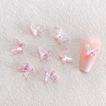 Detailed view of iridescent resin butterfly nail charms on a pink mannequin nail tip - Aurora Pink