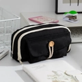 Black canvas pencil case with three zipper layers and wooden button detail on desk - Black