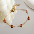 Détail d'un bracelet doré à double chaîne avec cinq cœurs roses et un fermoir mousqueton - Cœur Rouge