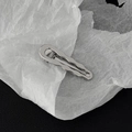 Détail de la pince à cheveux ondulée en métal argenté avec finition miroir sur fond texturé - Style Vague Argent