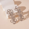 Detail view of silver metal floral drop earrings on a stylish white wavy display stand - Silver