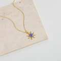 Golden sun pendant necklace with purple center stone displayed on a beige stone block - Purple