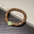 Pulsera de cuentas de madera marrón con piedra jade sobre papel de caligrafía zen - Sándalo Verde Estilo Ábaco