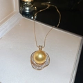 Detailed close-up of a large gold pearl pendant with crystal accents in a jewelry box - Necklace - Gold