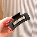 Large matte black square hollow hair claw clip for women held against a textured wall - Large Rectangle