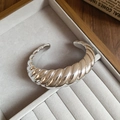 Macro detail of silver croissant twist bangle with a polished mirror finish on jewelry tray - Bracelet-Silver-Ribbed
