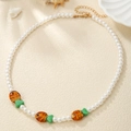 Detail of colorful beaded fish necklace with pearls and sea charms on a beige surface - White Pearl Orange Green Fish