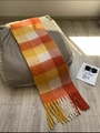 Maillard style orange and yellow plaid winter scarf with thick fringes on a sofa - AC Plaid Orange Red