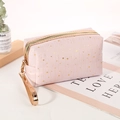 Pink cosmetic bag with gold star patterns and a matching wrist strap on an open book - Light Pink