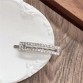 Close-up of a silver rectangular hair clip with inlaid rhinestones on a ceramic dish - Rectangle / White