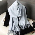 Soft light blue cashmere-style scarf with fringe tassels draped over black sweater - Haze Blue