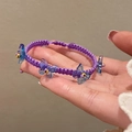 Détail d'un bracelet tressé violet avec des breloques papillon bleues et des perles dorées - Style Papillon Tissé Violet