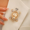 Elegante broche de tortuga dorada con gema y pedrería en la solapa de un traje beige - Blanco