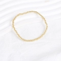 Detail of minimalist golden bead strand bracelet laid on a white textured fabric surface - Gold