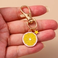 Golden lemon slice keychain with yellow enamel charm and star pendant on pink background - Pink