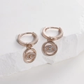Close-up of rose gold evil eye earrings with pavé crystals on a textured stone surface - Rose Gold - White Zirconia