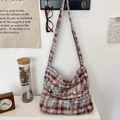 Detailansicht der rot-blauen Karo-Canvas-Tasche mit Knopfklappe und gewebtem Markenetikett - Blau