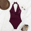 Flat lay of burgundy halter one-piece swimsuit with ruched waist on marble surface - Deep purple