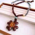 Détail d'un pendentif fleur en cuir artisanal avec un collier en laine tissée texturée - Style de Corde Tissée Brun Rouge / Marron
