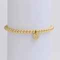 Close-up of golden beaded stretch bracelet with letter O charm on white pedestal - Letter O (DB240603-O)