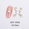 Macro shot of 6x10mm gold alloy bow and teardrop crystal nail art gems on white sand - Gold Bowknot Water Drop White Crystal Style (8906)