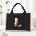 Black linen tote bag featuring a gold letter L with colorful floral print and woven trim - Bronze Floral Letter L
