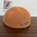 Brown wool beret hat with metallic logo plate on a rustic wooden surface background - Caramel color