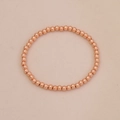 Dettaglio del bracciale a sfere in oro rosa con perle metalliche lucide su sfondo beige - Bracciale a Perline Oro Rosa