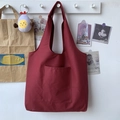 Minimalist burgundy canvas tote bag with front pocket hanging on a white wall hook - Red