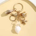 Close-up of golden keychain with luminous seashell and starfish pendants on beige background - White