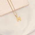 Detailed view of gold necklace featuring letter H pendant with dot texture on stone - Letter H