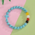 Dettaglio del bracciale con perline blu, ciondolo a croce e perline colorate - Turchese