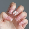 Close-up of elegant nude French press-on nails with 3D white ribbon bow accents - French White Bow