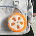 Plush orange slice coin purse and keychain accessory attached to a blue backpack - Orange