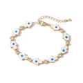 Detailaufnahme des goldenen Hamsa-Armbands mit blauem Emaille-Auge und Zirkonia-Steinen - Weiß