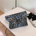 Dettaglio di un'elegante trousse per cosmetici in jacquard floreale su un tavolo bianco - Nero con rami blu-bianchi