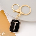 Macro shot of letter T rhinestone keychain with black enamel finish and golden hardware - Letter T