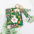 Detail view of a floral green card holder with gold ring and tassel charm on white background - Green Floral