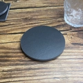 Detail view of round black natural slate coaster on wooden table with glass cup - Straight Edge Round Style