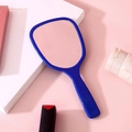 Blue handheld makeup mirror with sleek plastic handle over soft pink vanity background - Dark Blue