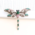 Vintage bronze dragonfly brooch with colorful rhinestones on a background of book pages - Green